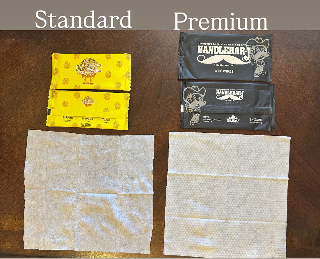 Standard wipe next to a Premium wipe, each with its printed packet. The Standard sheet is smooth and flat. The Premium sheet has a raised honeycomb texture.
